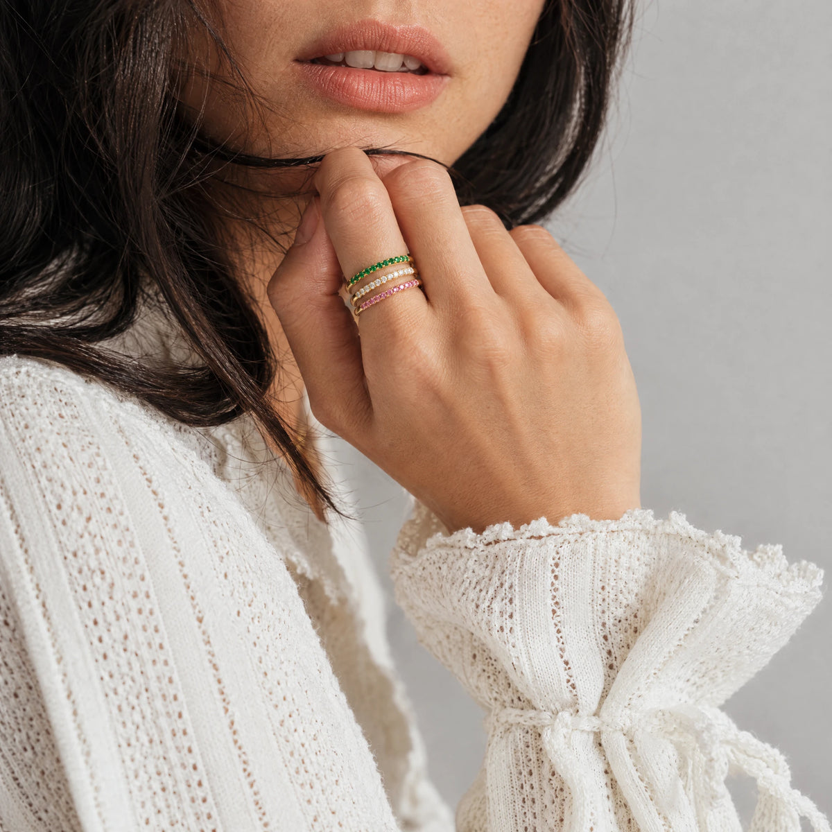 Woman's hand near her chin wearing three stacked gold Nora Birthstone Stacking Rings in green, clear and pink