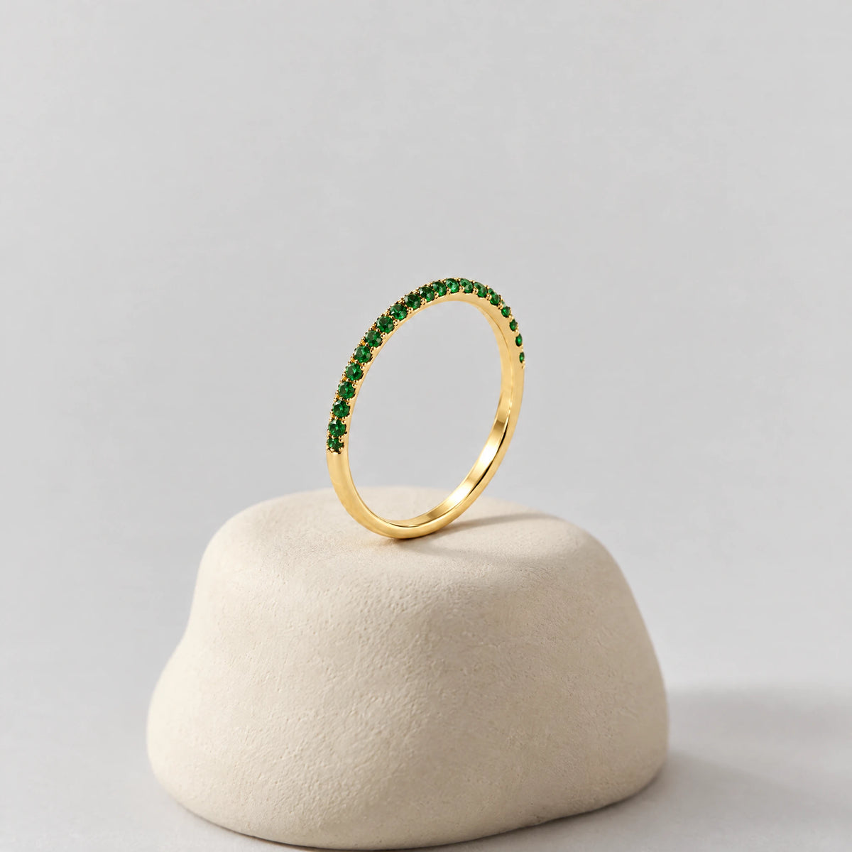 Gold Nora Birthstone Stacking Ring with green stones on a cream clay pedestal