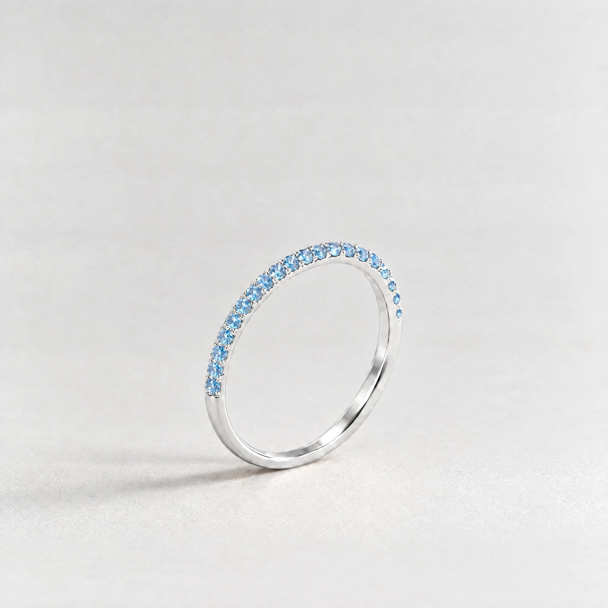 Silver Nora Birthstone Stacking Ring with aquamarine blue March birthstone-color crystals on a light grey background