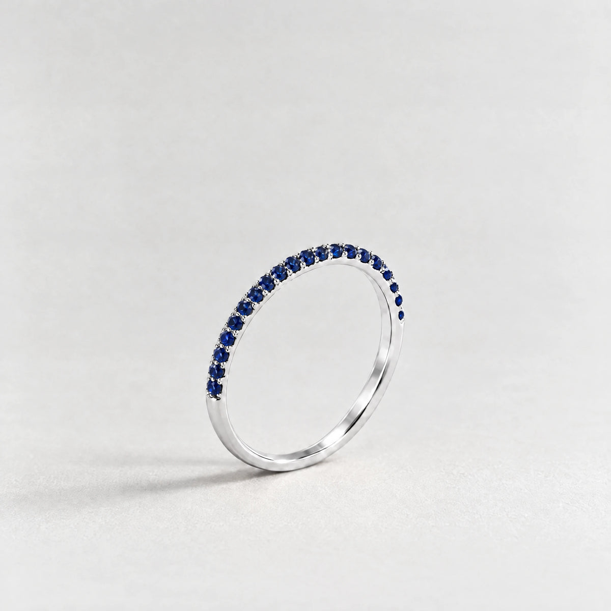 Silver Nora Birthstone Stacking Ring with sapphire blue September birthstone-color crystals on a light grey background