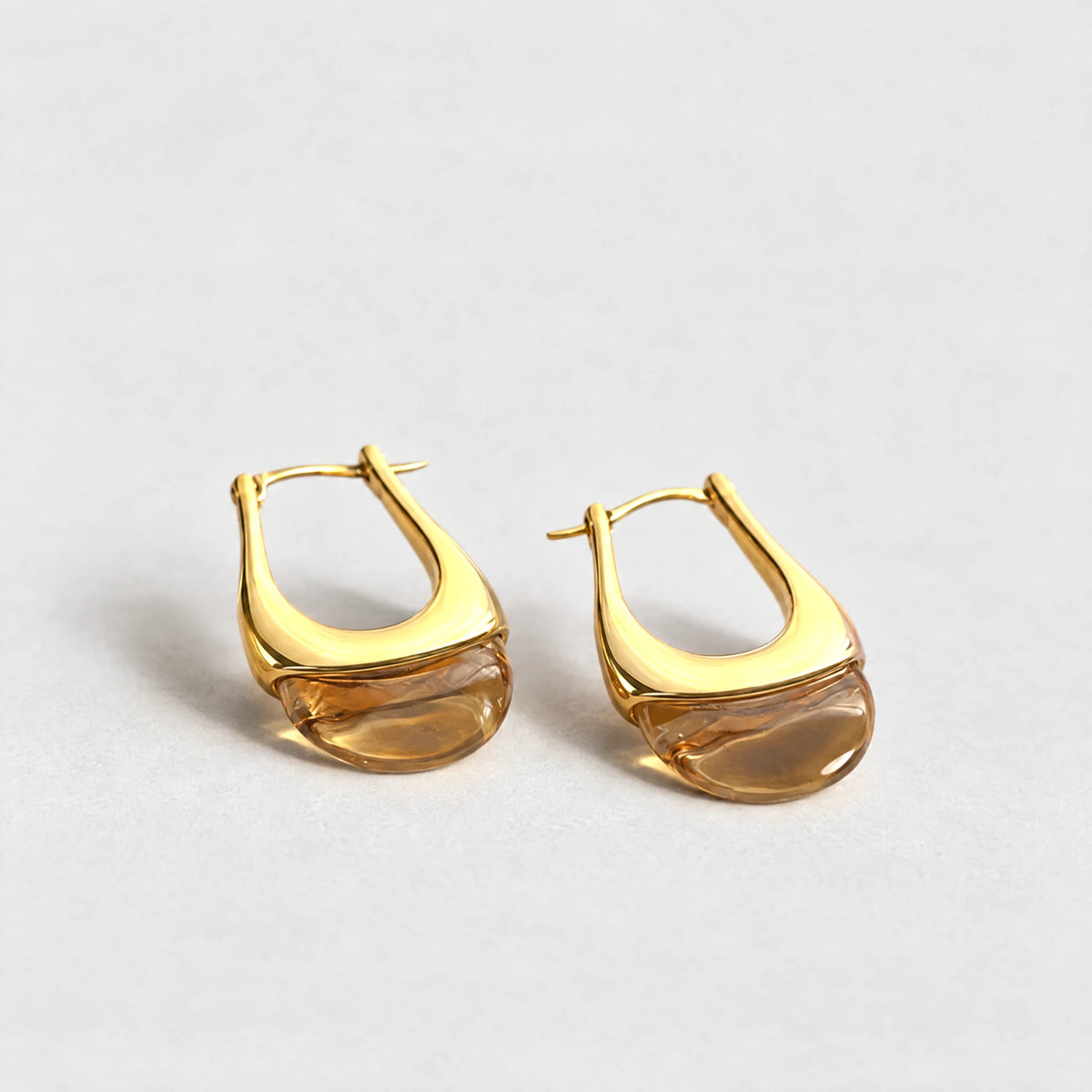 Gold Pia U-Shape Hoop Earrings with an amber translucent inset on a light grey background