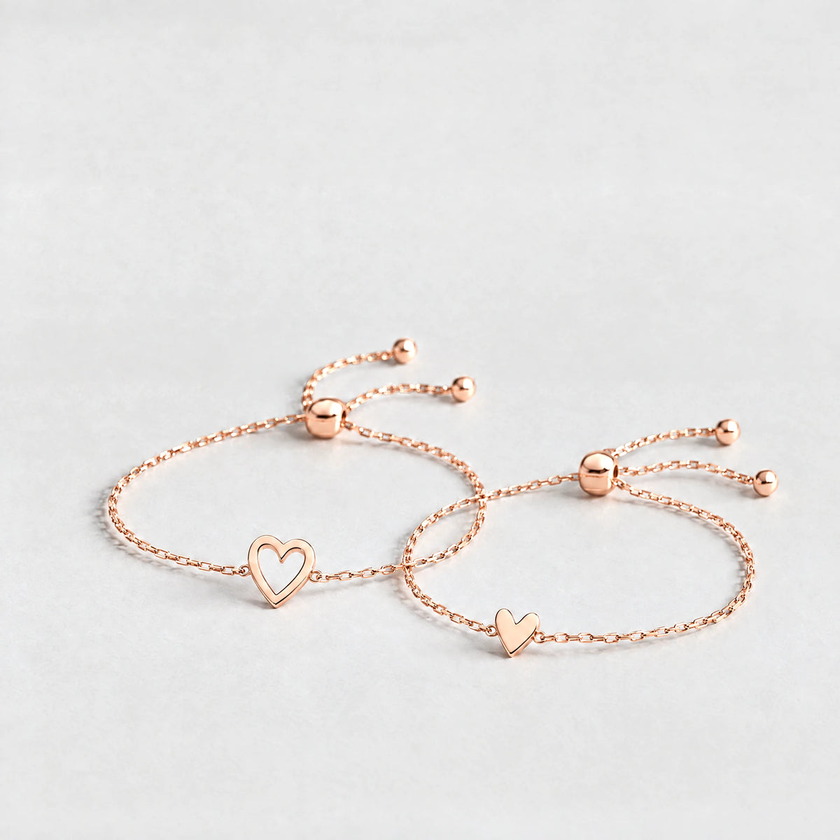 Rose gold Rosie Two Hearts Bracelet Set with an open heart and a small solid heart on a light grey background