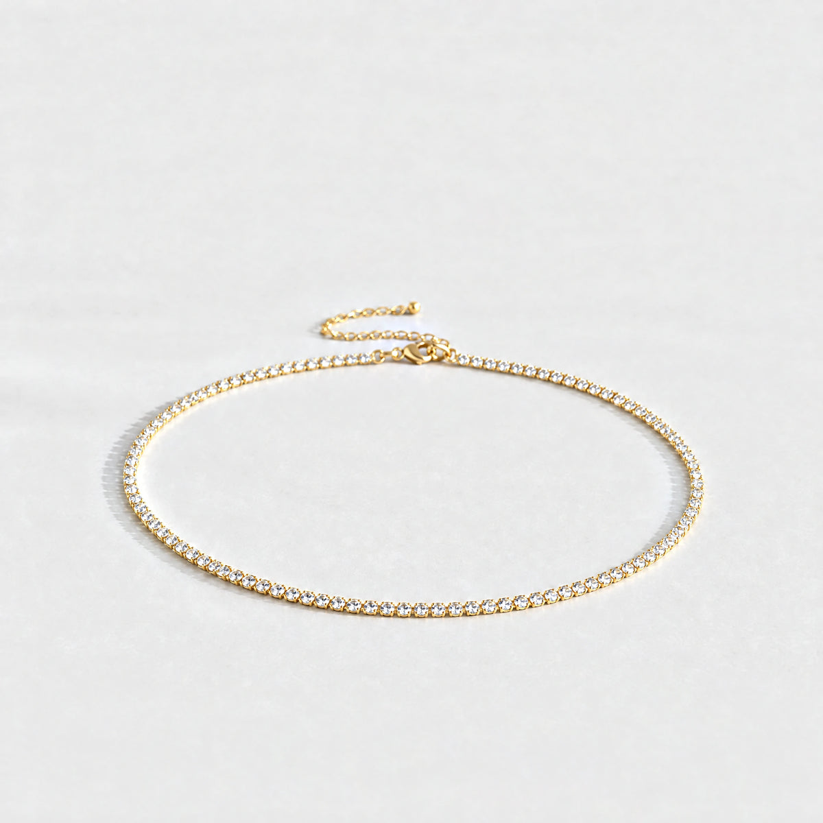 Gold Tessa Birthstone Tennis Necklace with crystal clear April birthstone-color crystals on a light grey background