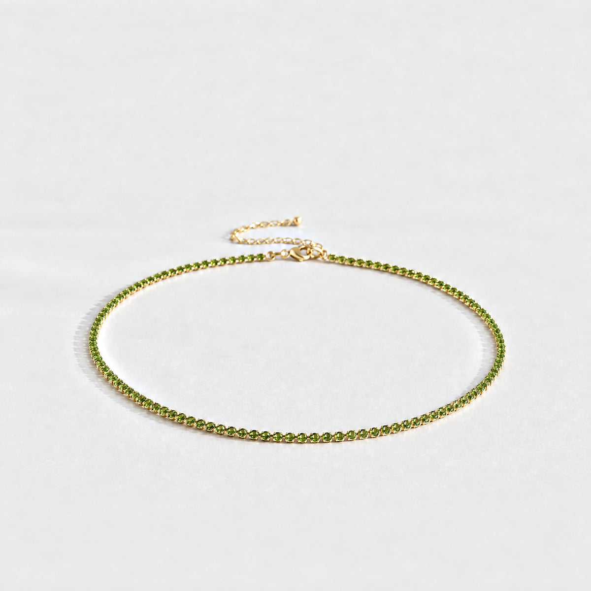 Gold Tessa Birthstone Tennis Necklace with peridot green August birthstone-color crystals on a light grey background