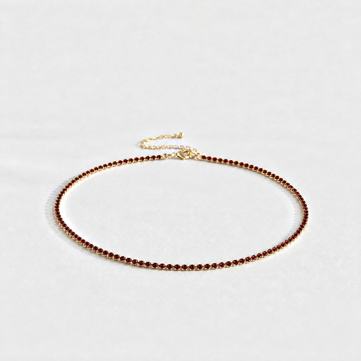 Gold Tessa Birthstone Tennis Necklace with garnet red January birthstone-color crystals on a light grey background