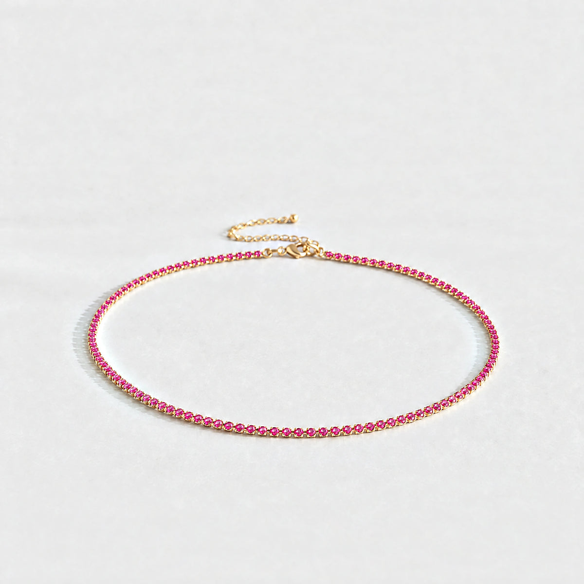 Gold Tessa Birthstone Tennis Necklace with ruby rose July birthstone-color crystals on a light grey background