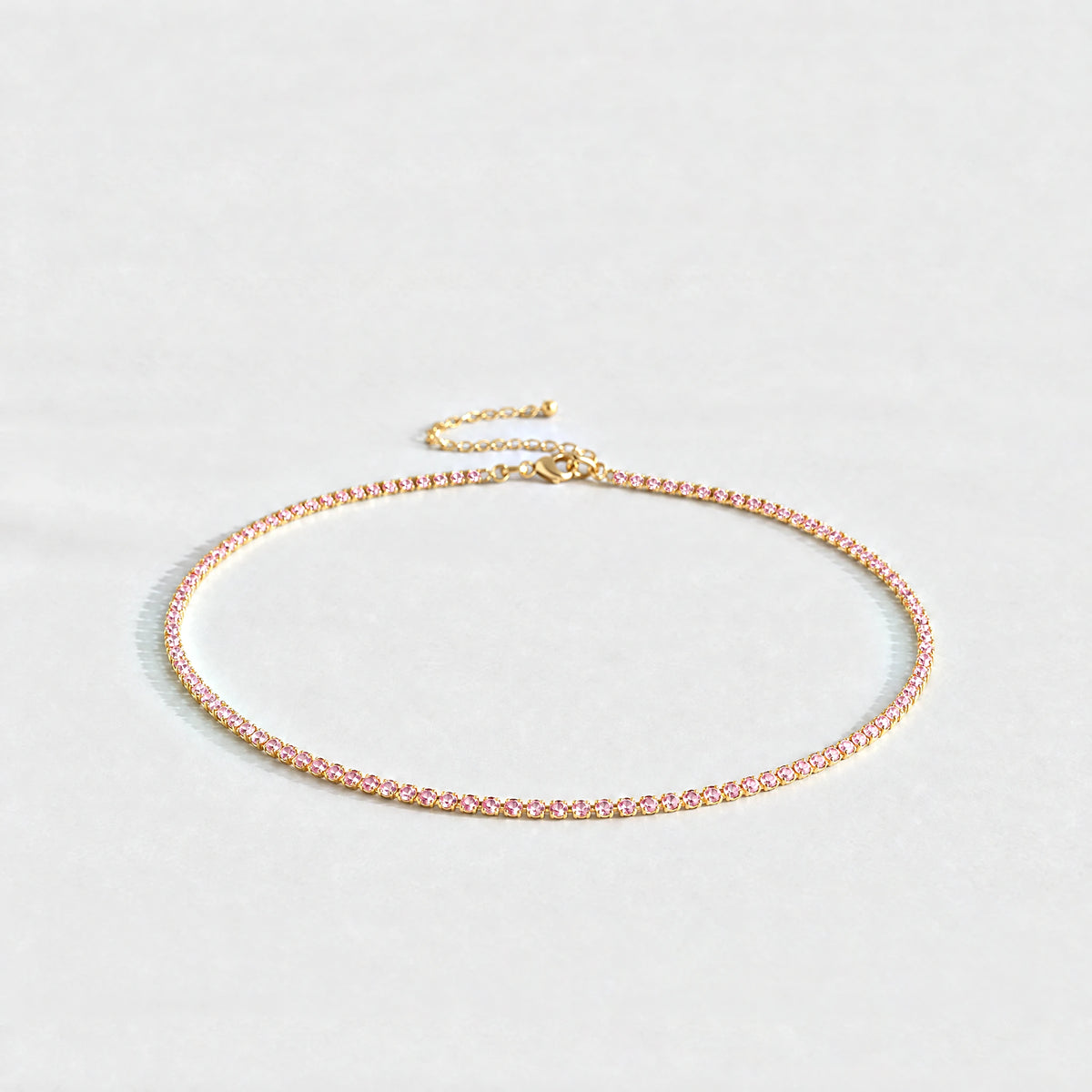 Gold Tessa Birthstone Tennis Necklace with tourmaline pink October birthstone-color crystals on a light grey background