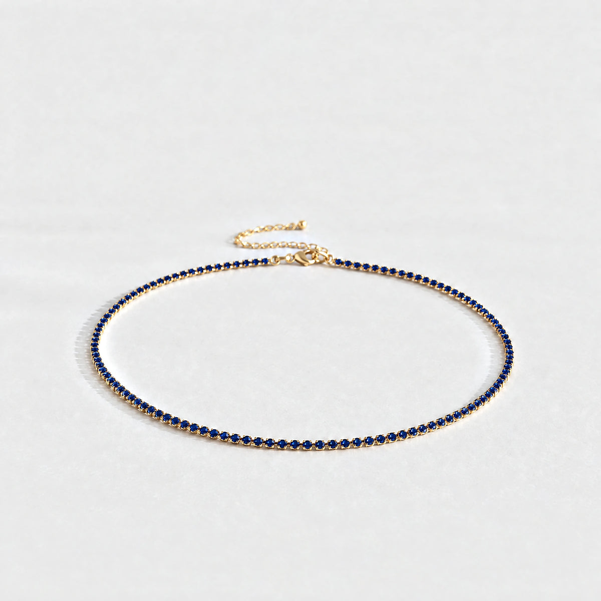 Gold Tessa Birthstone Tennis Necklace with sapphire blue September birthstone-color crystals on a light grey background