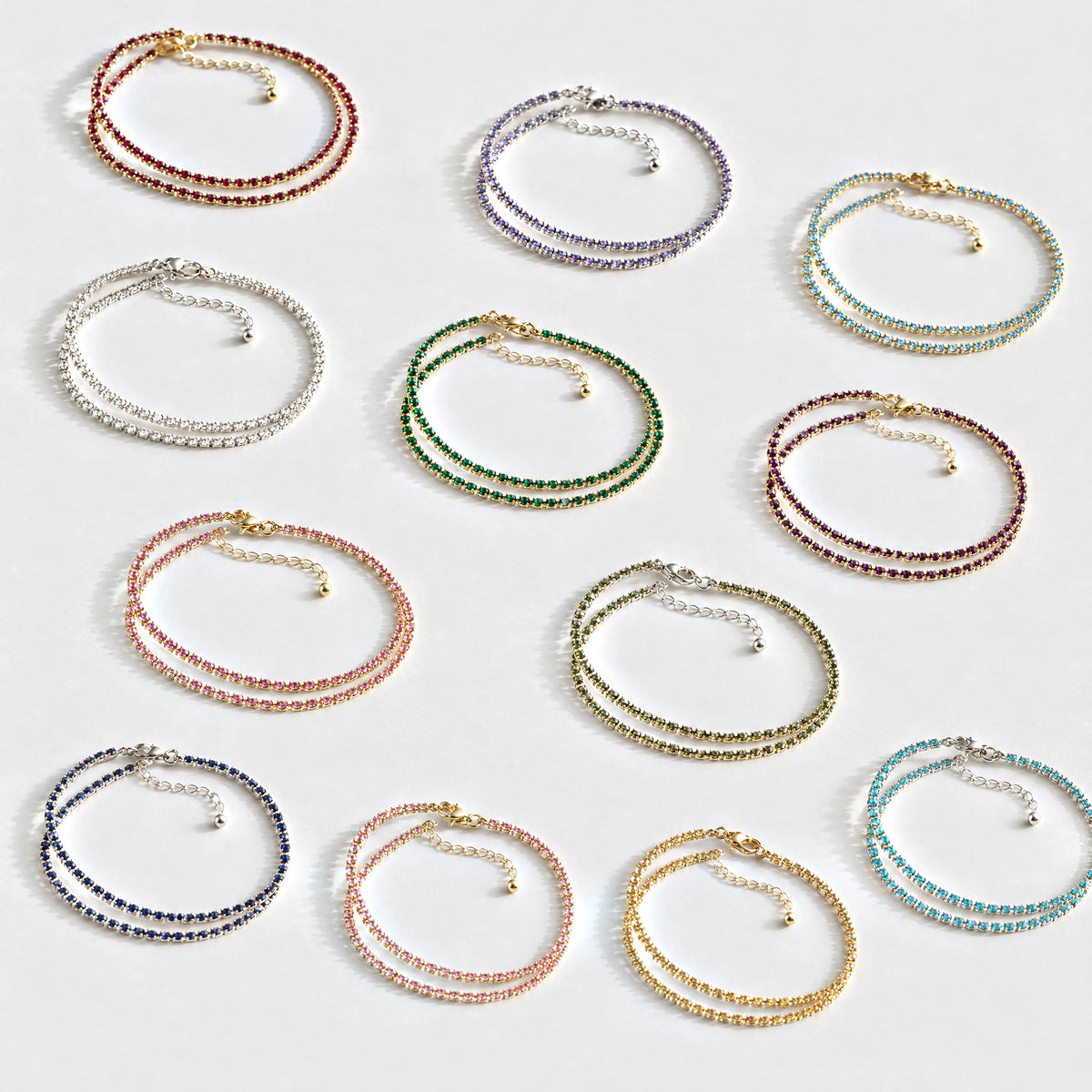 Twelve Tessa Birthstone Tennis Necklaces in every birth month color on a light grey surface