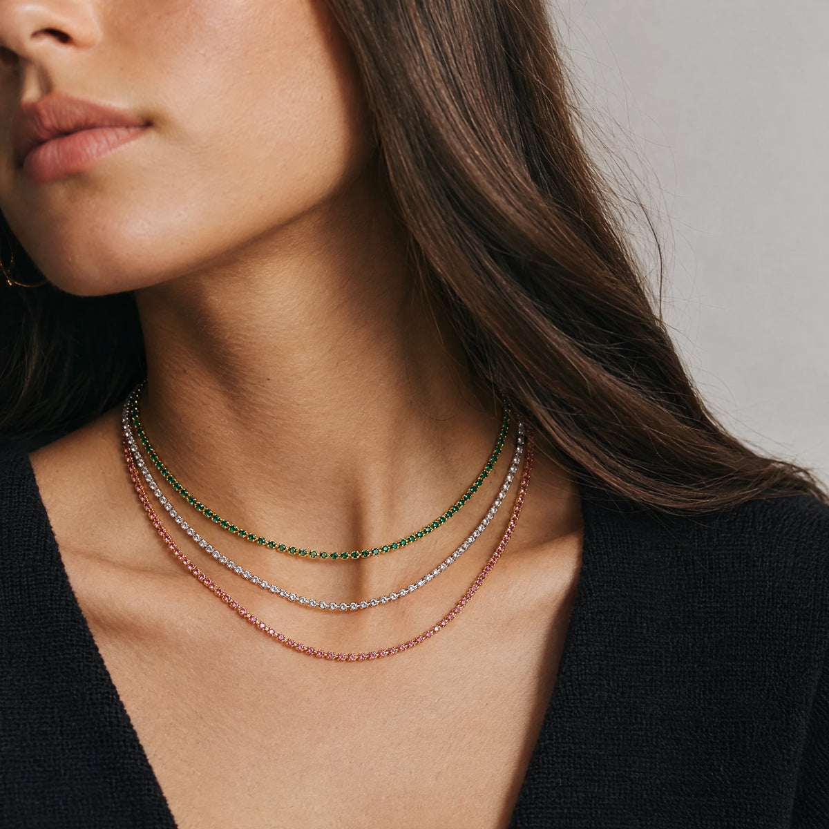 Three Tessa Birthstone Tennis Necklaces layered on the neck in green, clear and pink