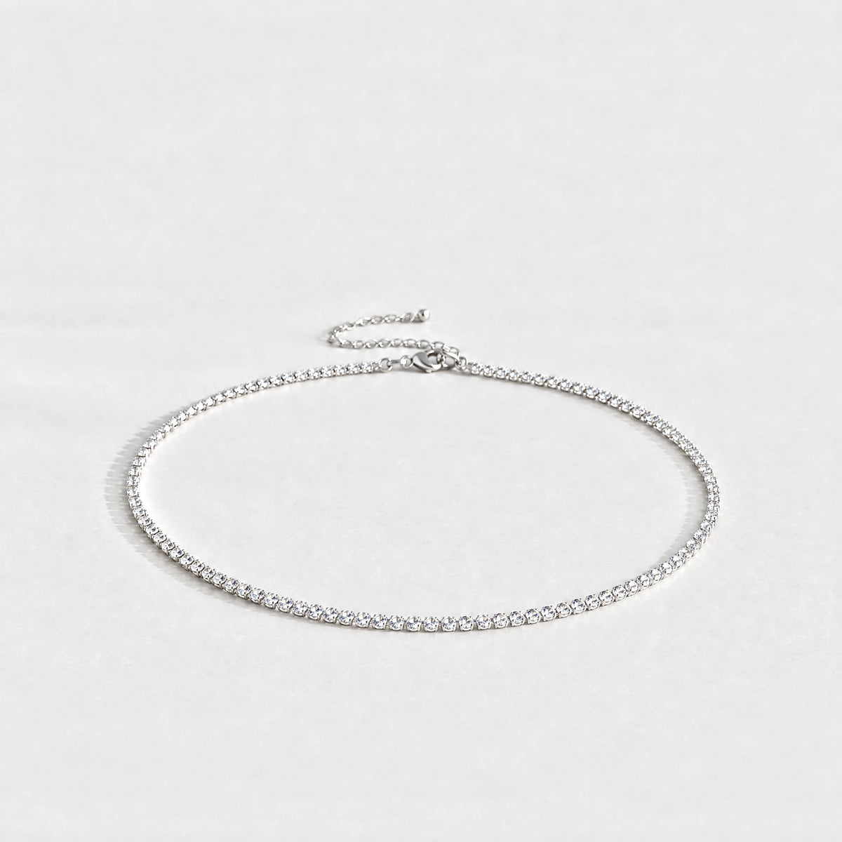 Silver Tessa Birthstone Tennis Necklace with crystal clear April birthstone-color crystals on a light grey background