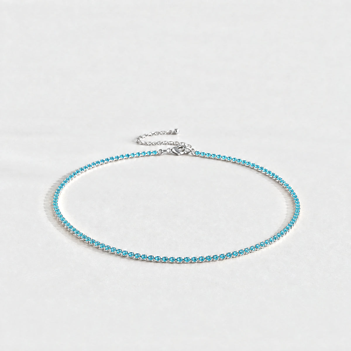 Silver Tessa Birthstone Tennis Necklace with topaz blue December birthstone-color crystals on a light grey background