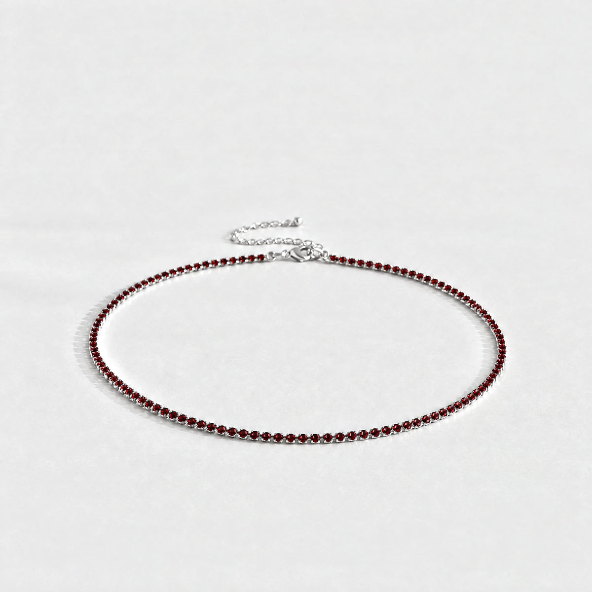 Silver Tessa Birthstone Tennis Necklace with garnet red January birthstone-color crystals on a light grey background