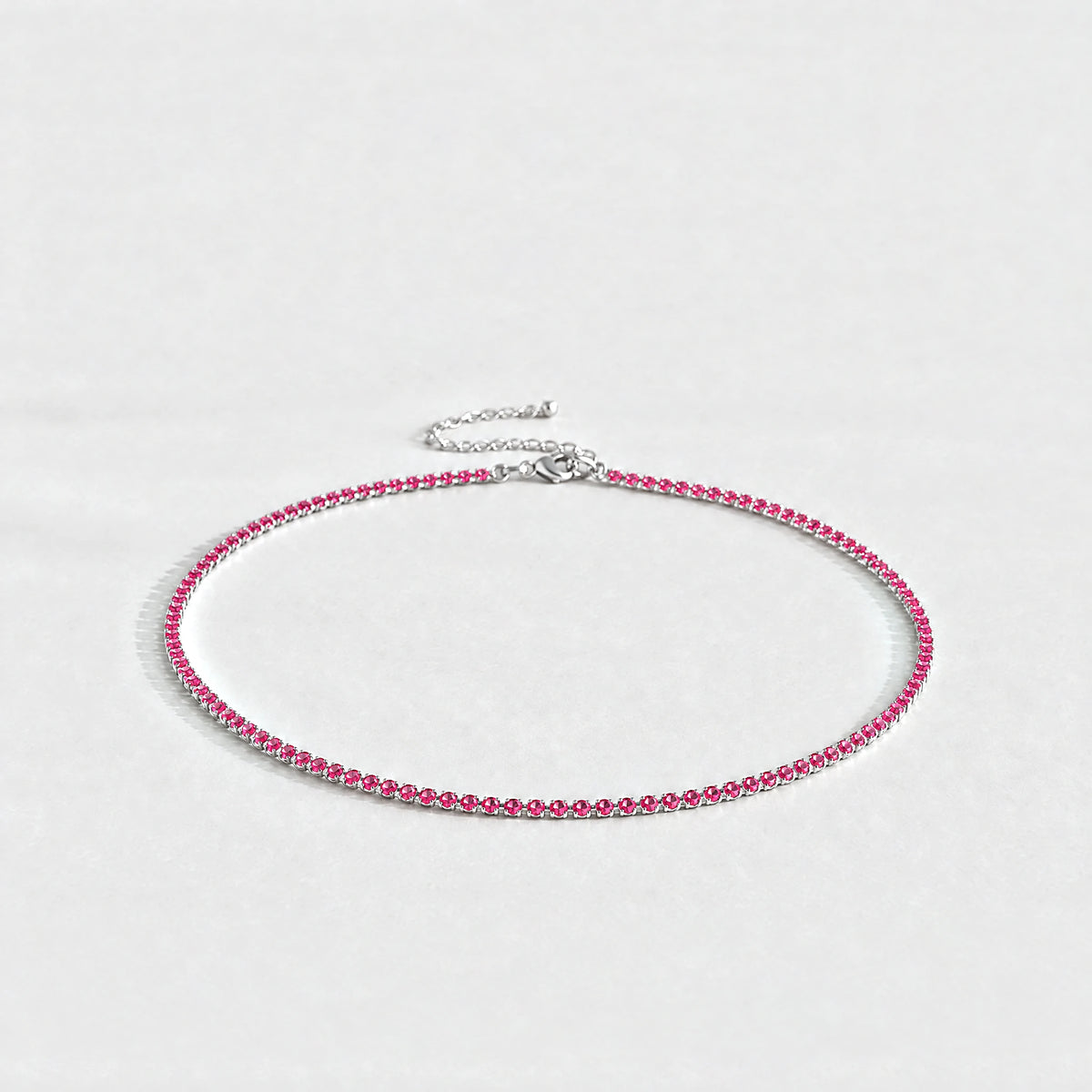 Silver Tessa Birthstone Tennis Necklace with ruby rose July birthstone-color crystals on a light grey background