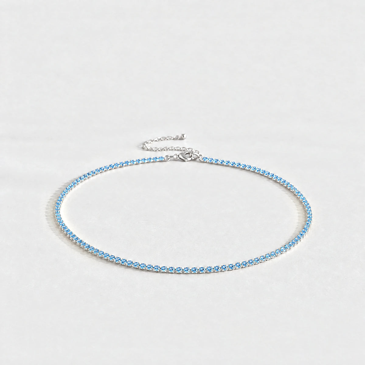 Silver Tessa Birthstone Tennis Necklace with aquamarine blue March birthstone-color crystals on a light grey background