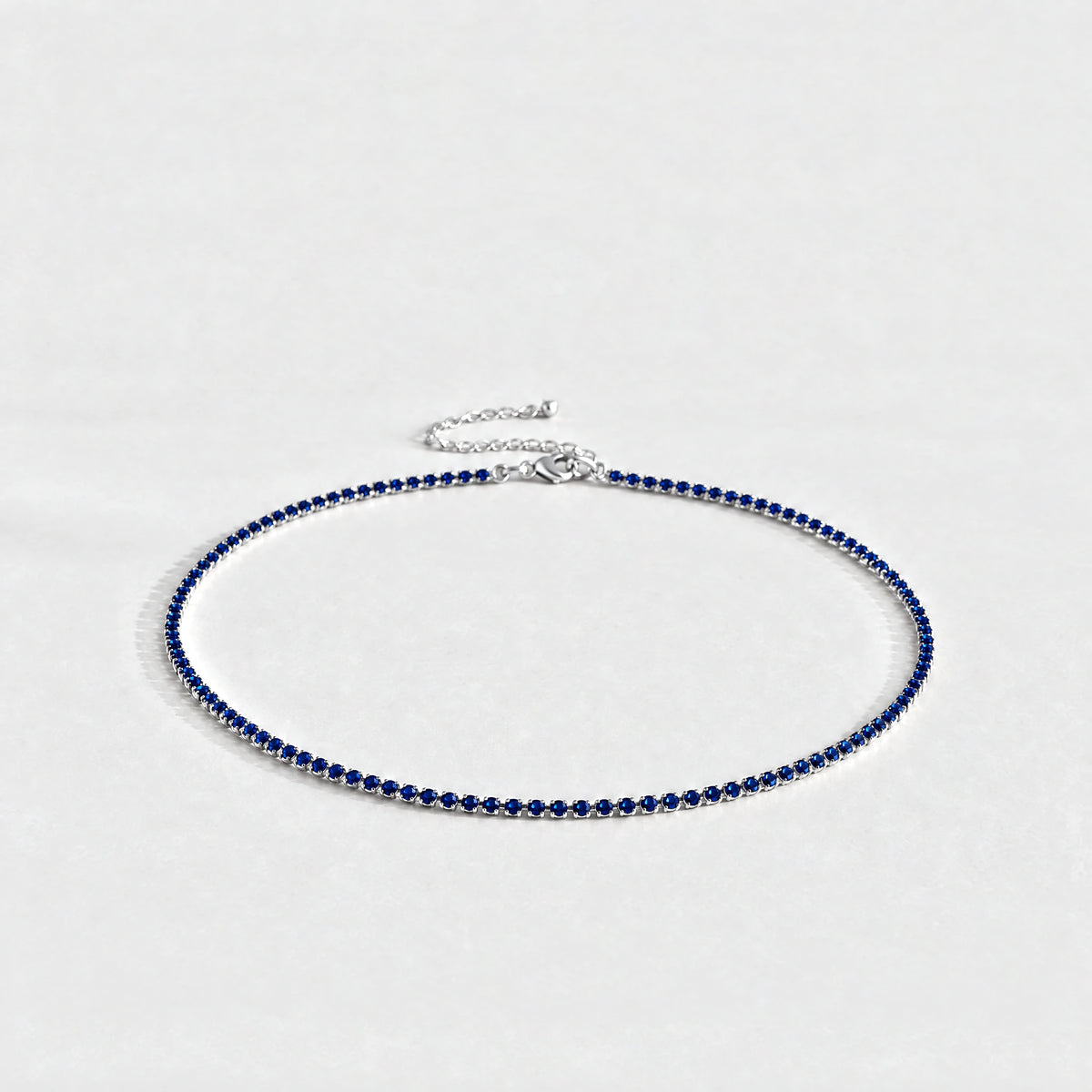 Silver Tessa Birthstone Tennis Necklace with sapphire blue September birthstone-color crystals on a light grey background