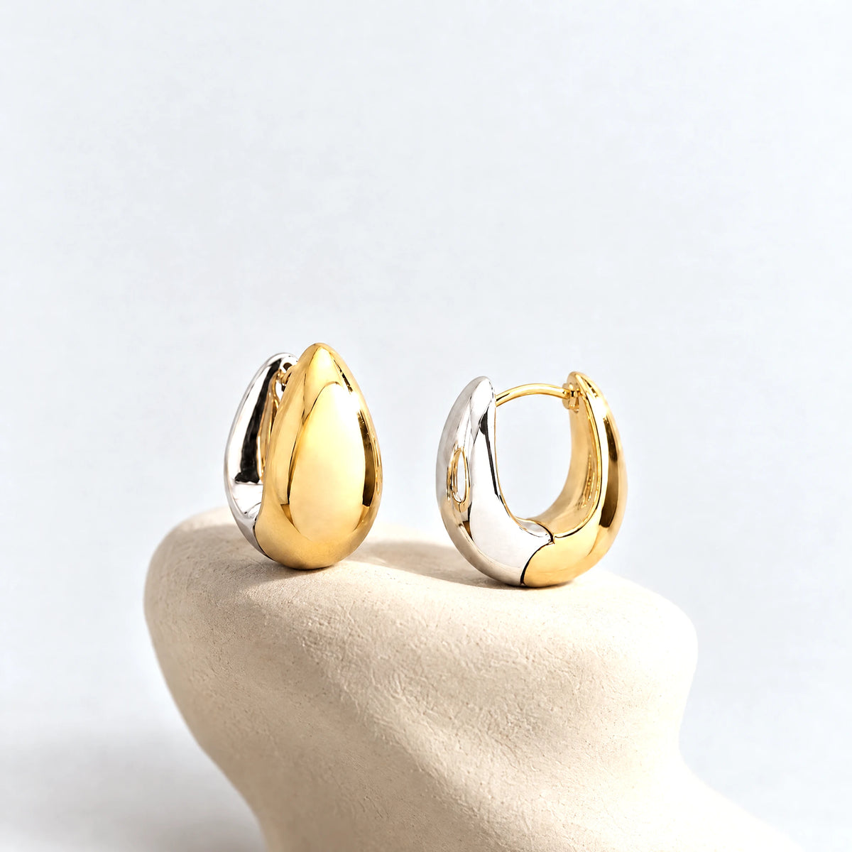 Vera Two-Tone Oval Hoop Earrings on a cream clay pedestal