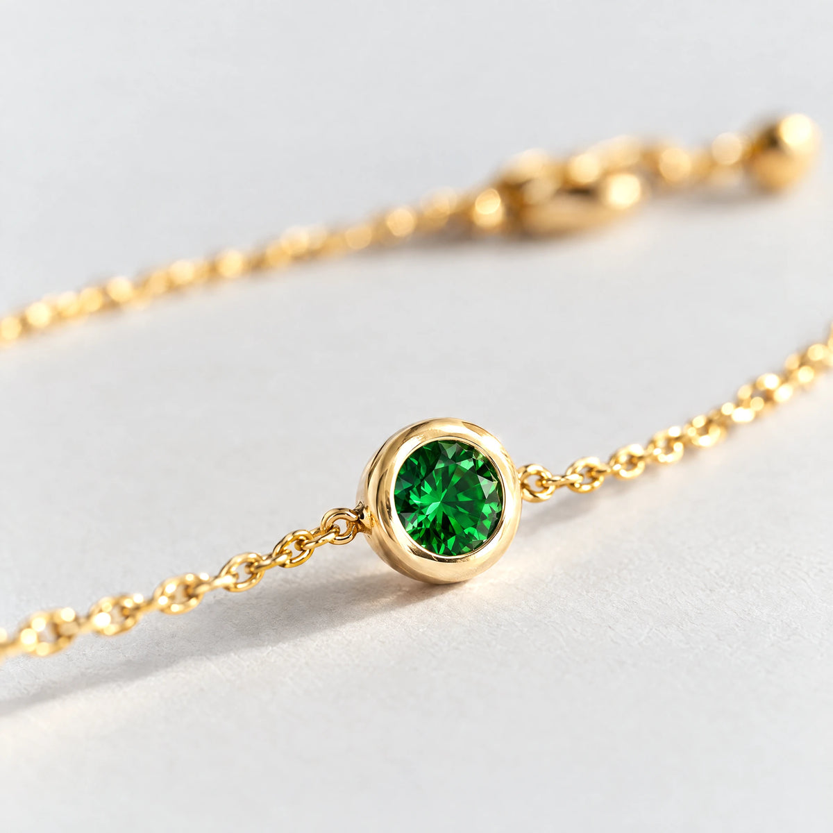 Close-up of the bezel-set emerald green stone on the gold Zara Birthstone Charm Bracelet