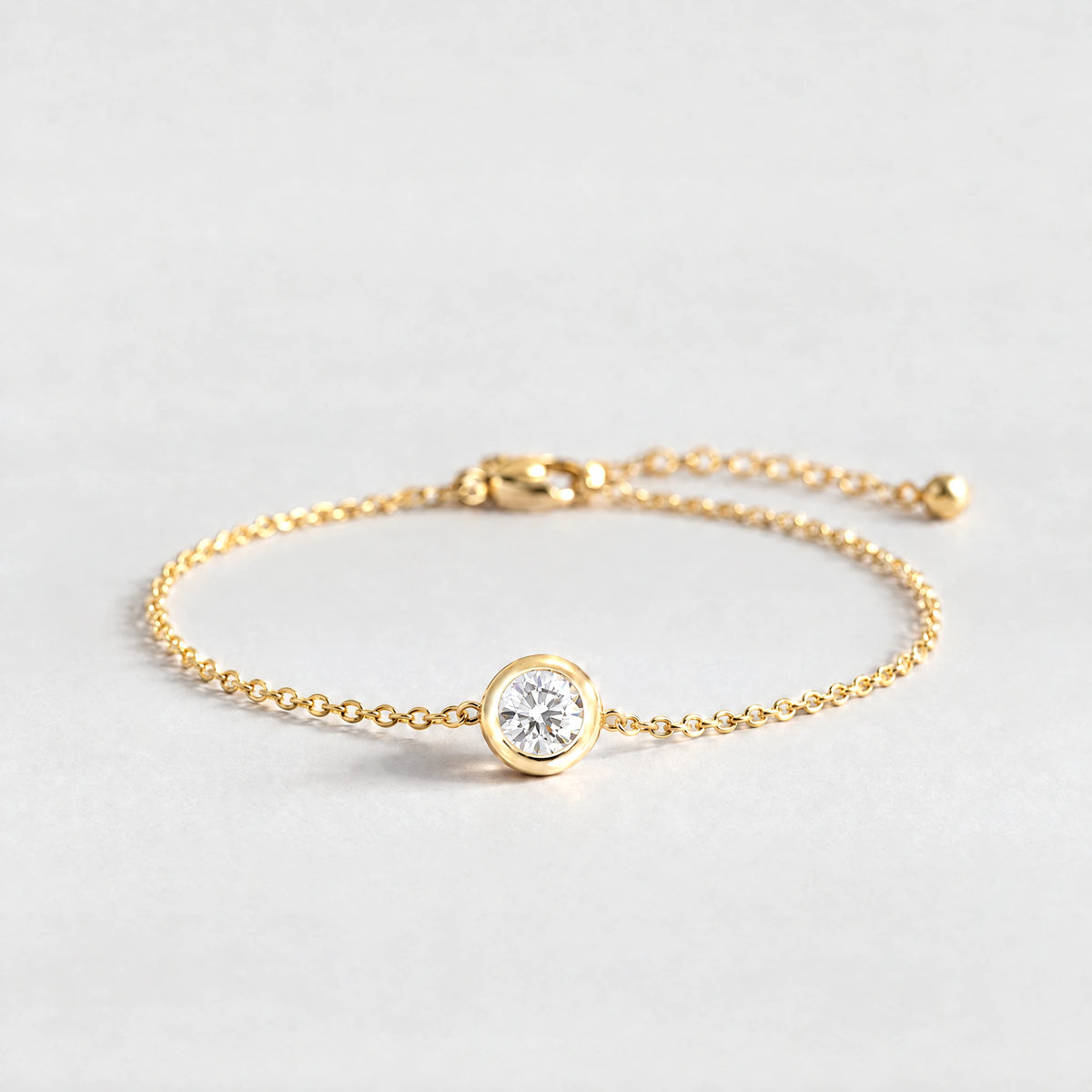 Gold Zara Birthstone Charm Bracelet with crystal clear April birthstone-color crystal on a light grey background