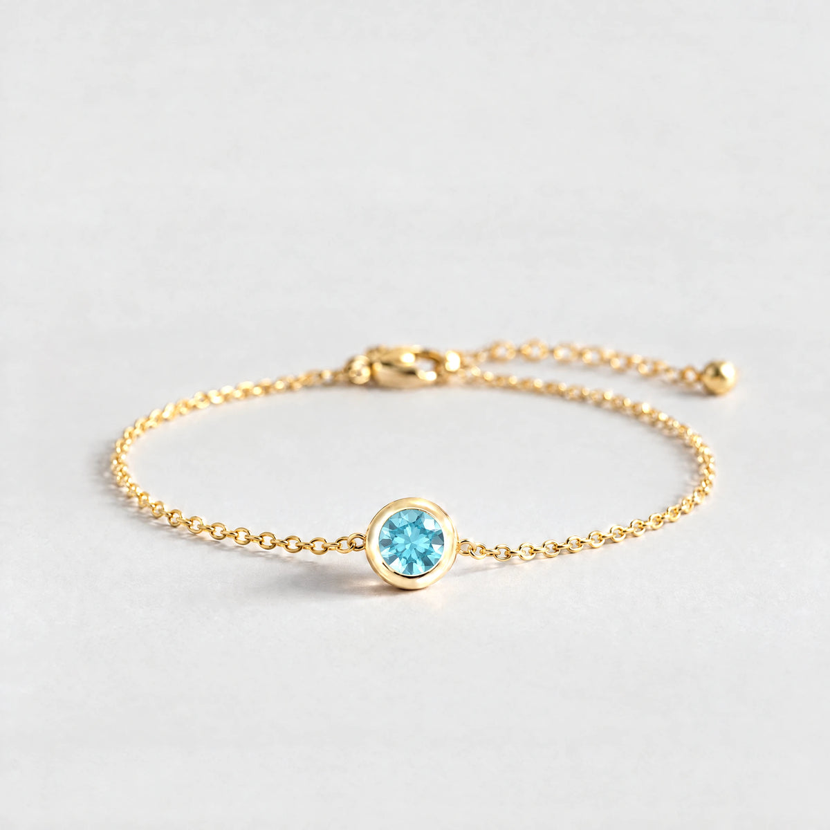 Gold Zara Birthstone Charm Bracelet with topaz blue December birthstone-color crystal on a light grey background