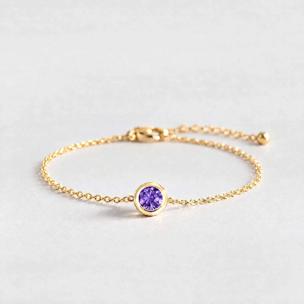 Gold Zara Birthstone Charm Bracelet with amethyst violet February birthstone-color crystal on a light grey background