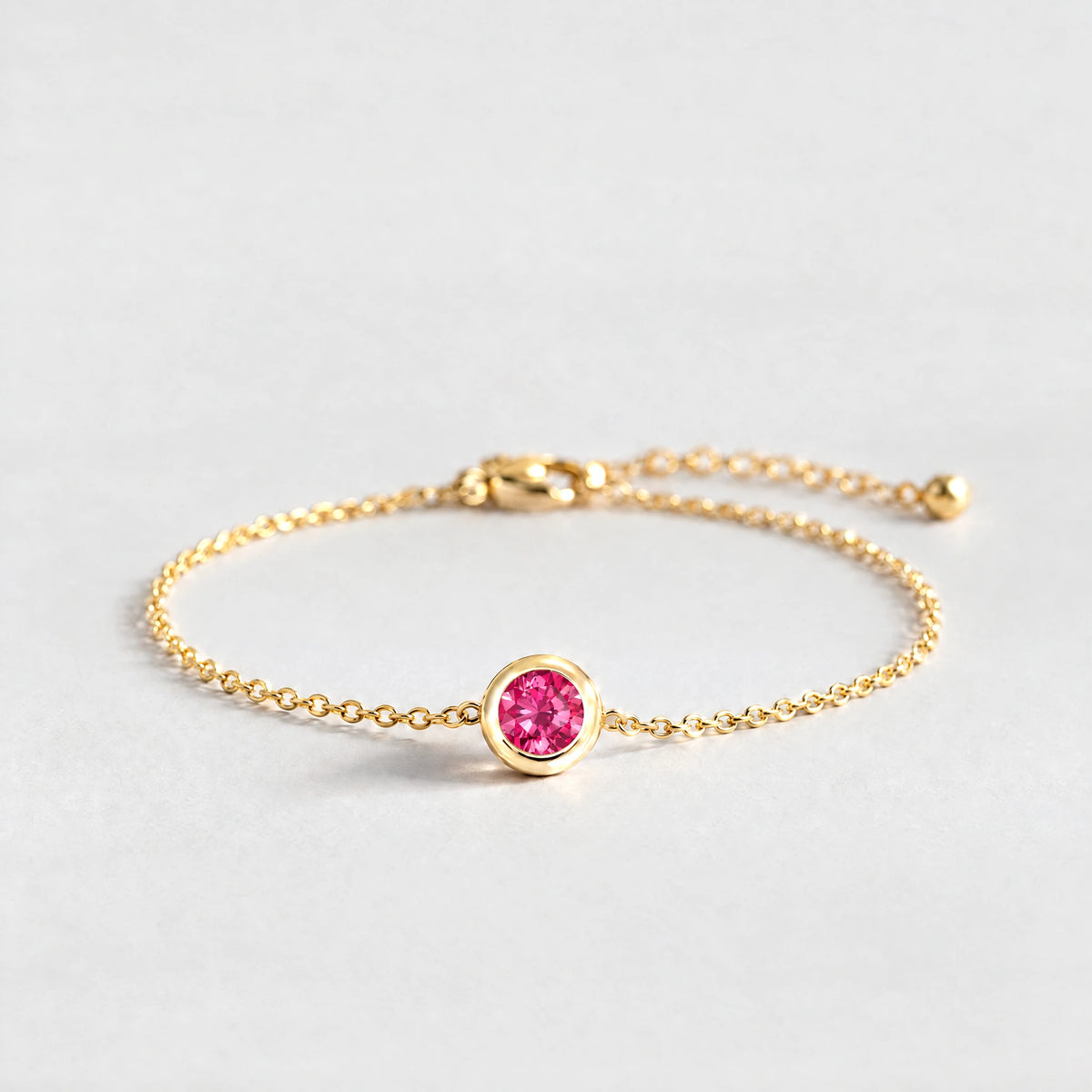 Gold Zara Birthstone Charm Bracelet with ruby rose July birthstone-color crystal on a light grey background