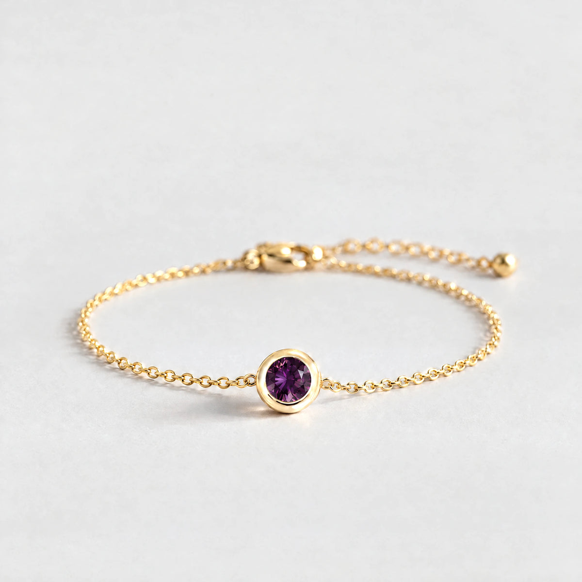 Gold Zara Birthstone Charm Bracelet with alexandrite plum June birthstone-color crystal on a light grey background