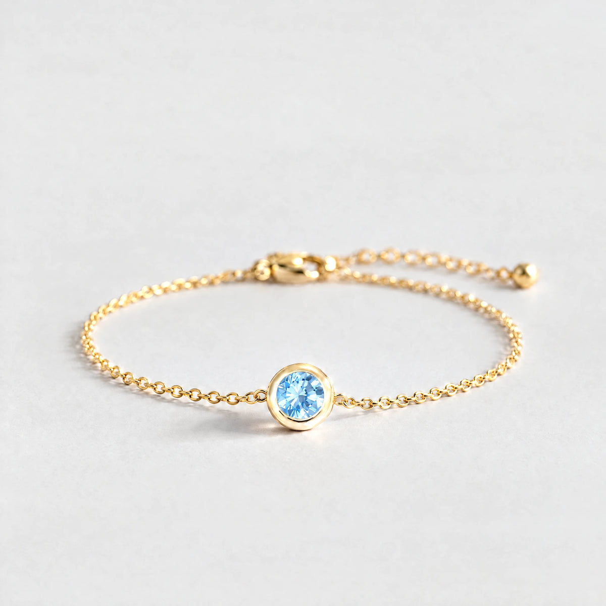 Gold Zara Birthstone Charm Bracelet with aquamarine blue March birthstone-color crystal on a light grey background