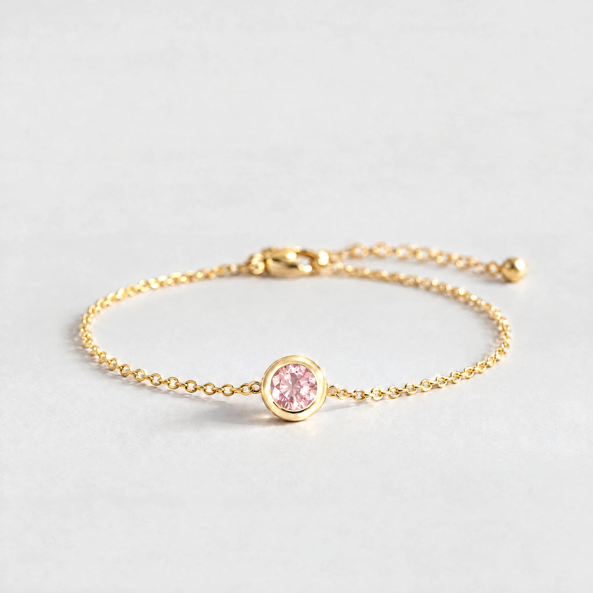 Gold Zara Birthstone Charm Bracelet with tourmaline pink October birthstone-color crystal on a light grey background