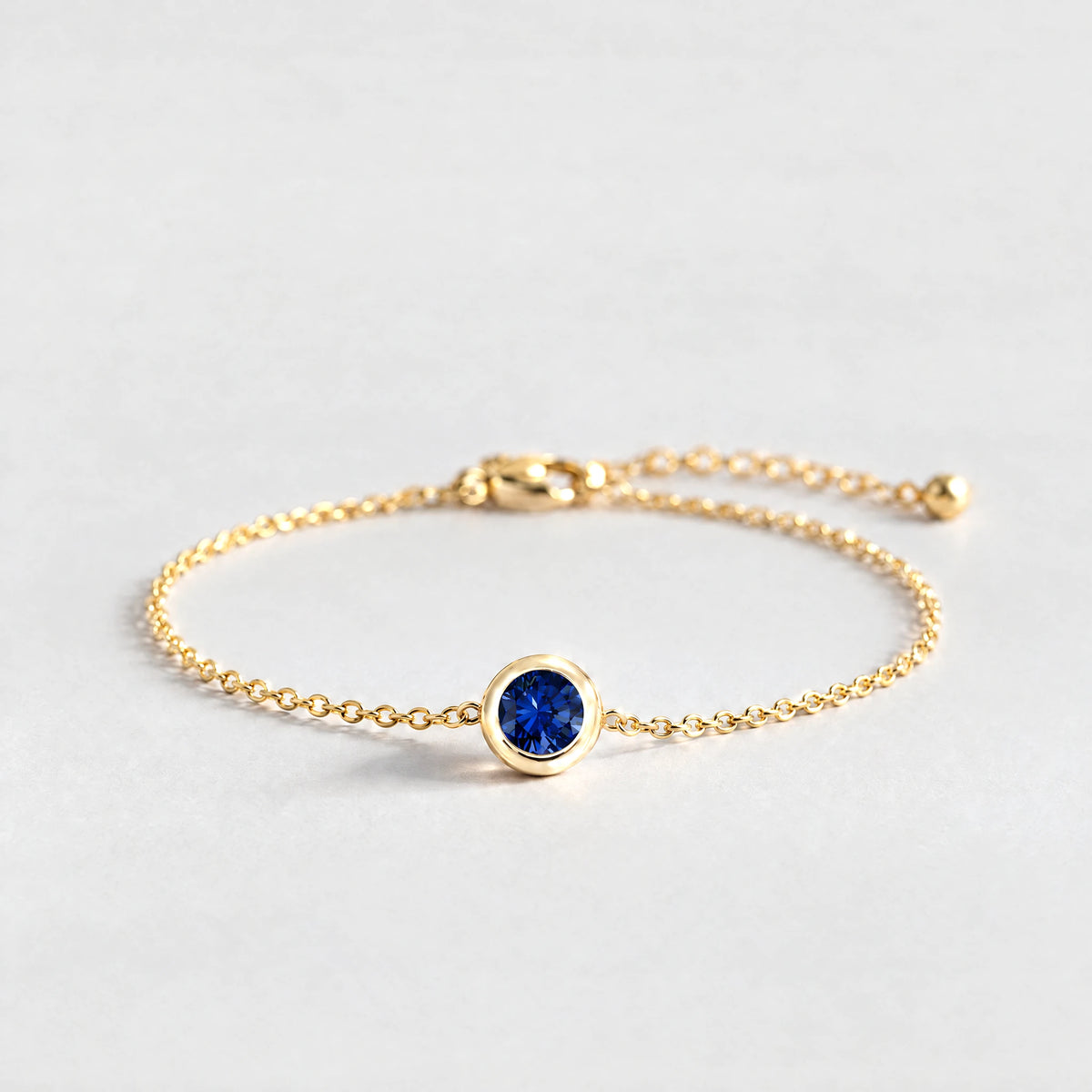 Gold Zara Birthstone Charm Bracelet with sapphire blue September birthstone-color crystal on a light grey background