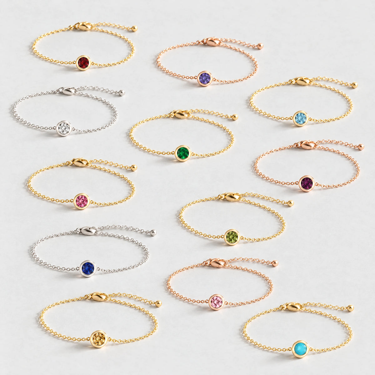 Twelve Zara Birthstone Charm Bracelets in every birth month color on a light grey surface