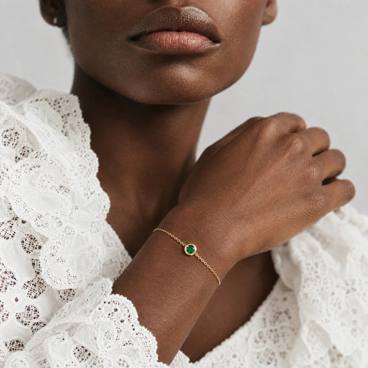 Woman's wrist wearing the gold Zara Birthstone Charm Bracelet with an emerald green stone