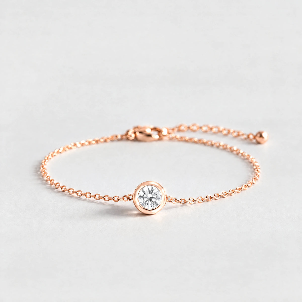 Rose gold Zara Birthstone Charm Bracelet with crystal clear April birthstone-color crystal on a light grey background