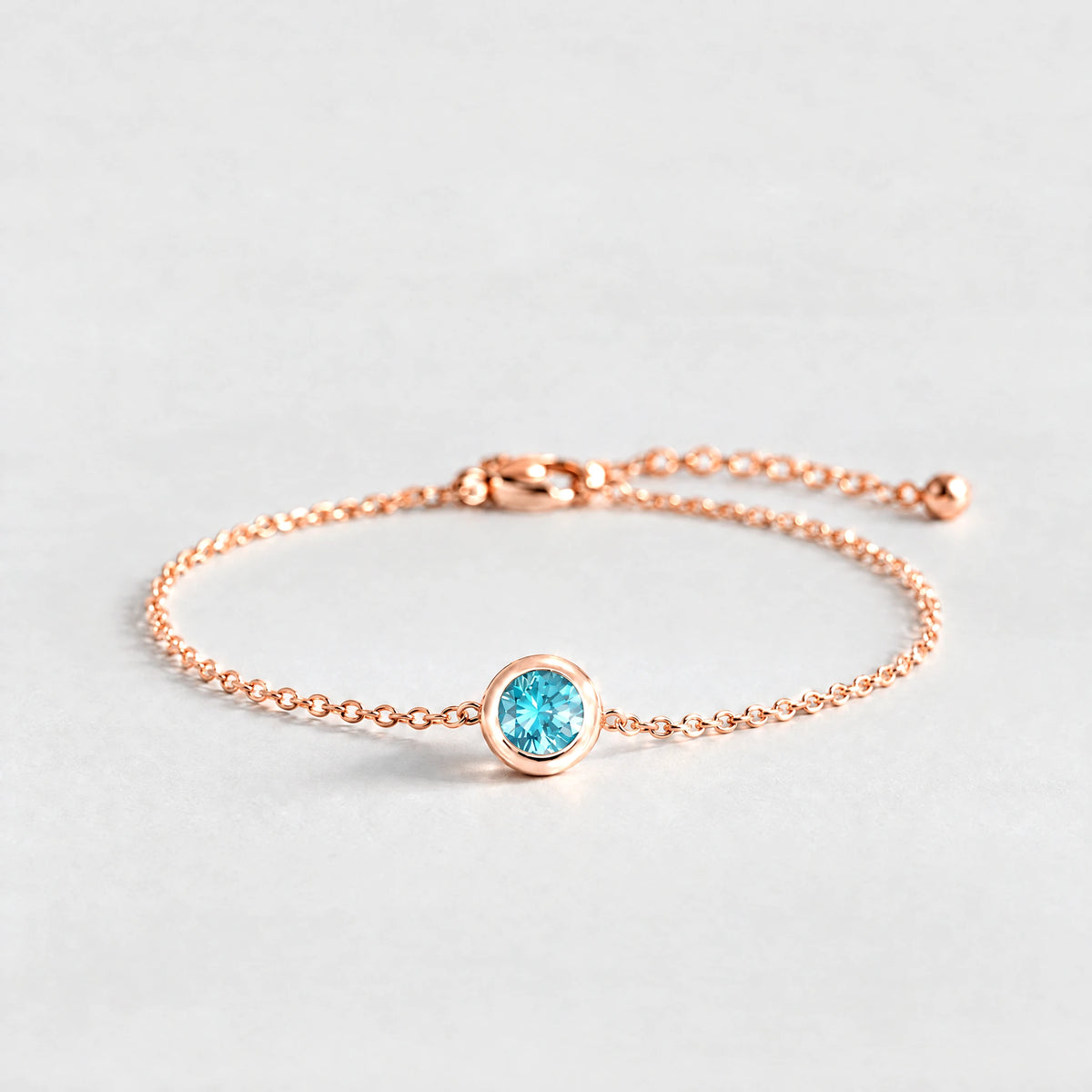 Rose gold Zara Birthstone Charm Bracelet with topaz blue December birthstone-color crystal on a light grey background
