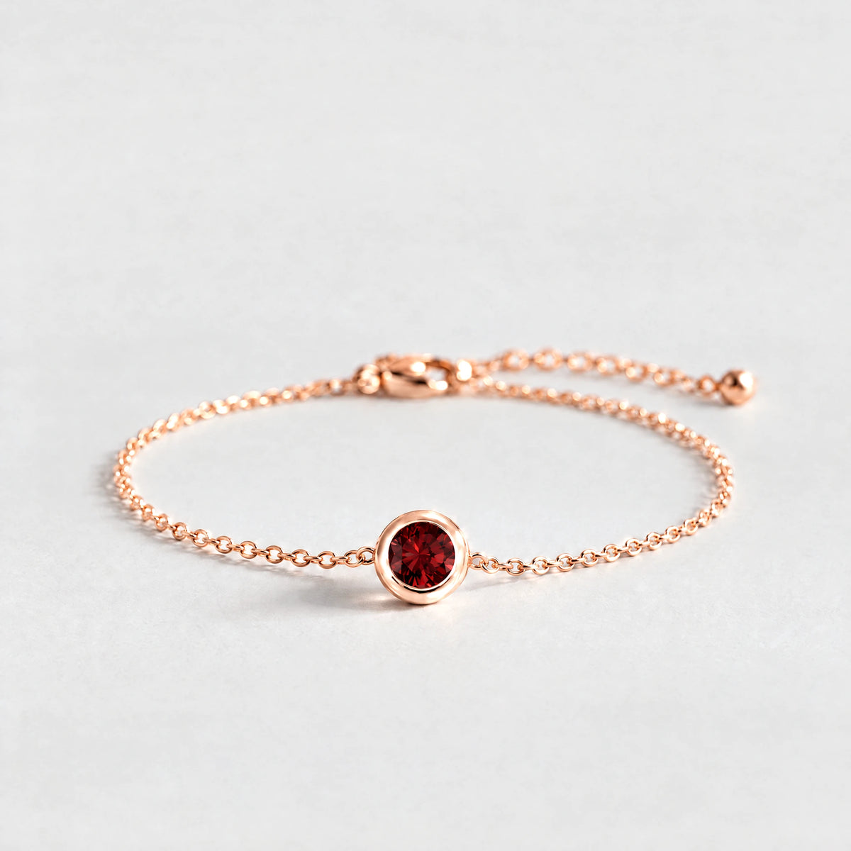 Rose gold Zara Birthstone Charm Bracelet with garnet red January birthstone-color crystal on a light grey background