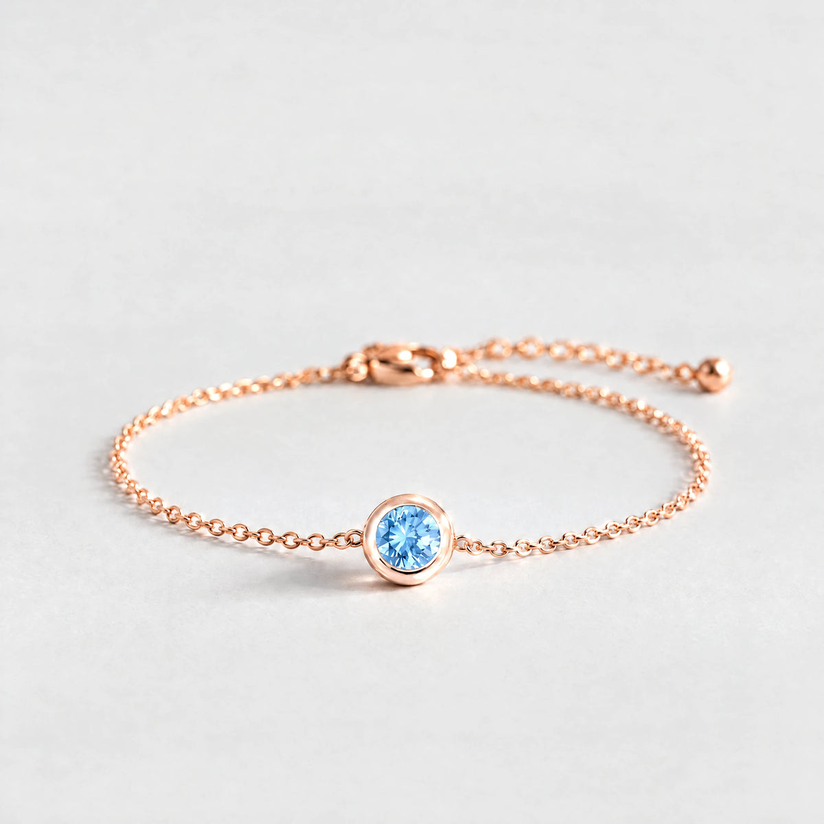 Rose gold Zara Birthstone Charm Bracelet with aquamarine blue March birthstone-color crystal on a light grey background