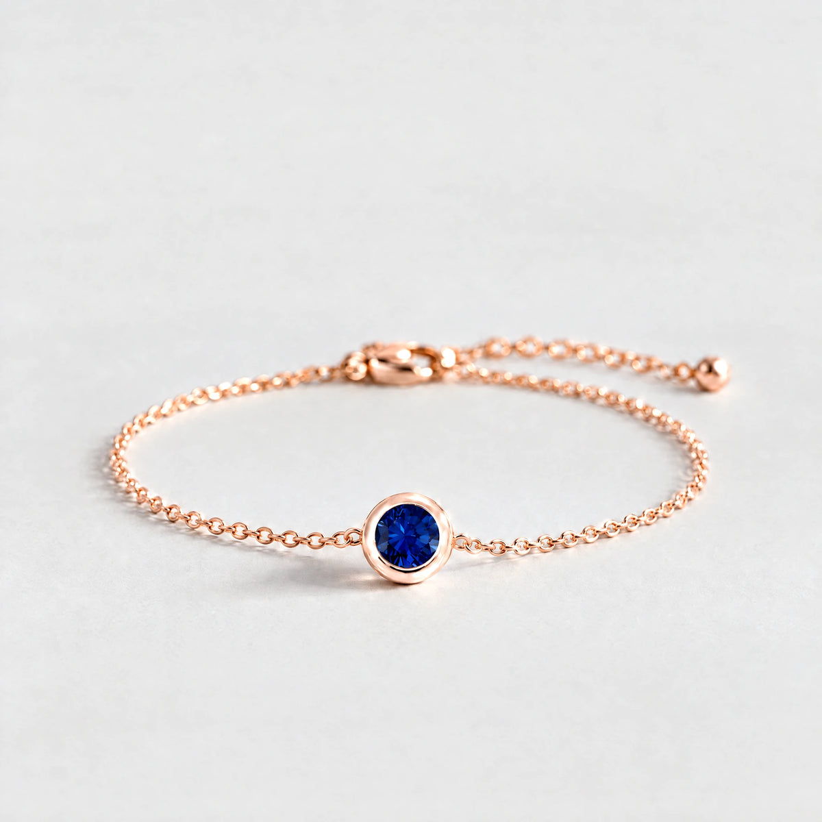 Rose gold Zara Birthstone Charm Bracelet with sapphire blue September birthstone-color crystal on a light grey background