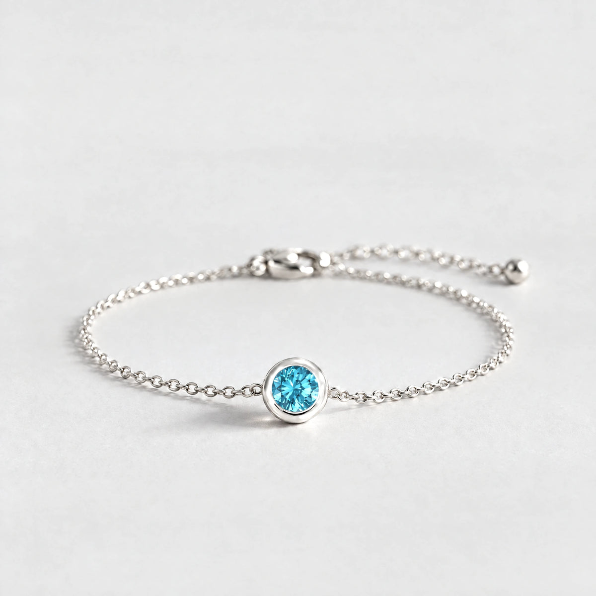 Silver Zara Birthstone Charm Bracelet with topaz blue December birthstone-color crystal on a light grey background