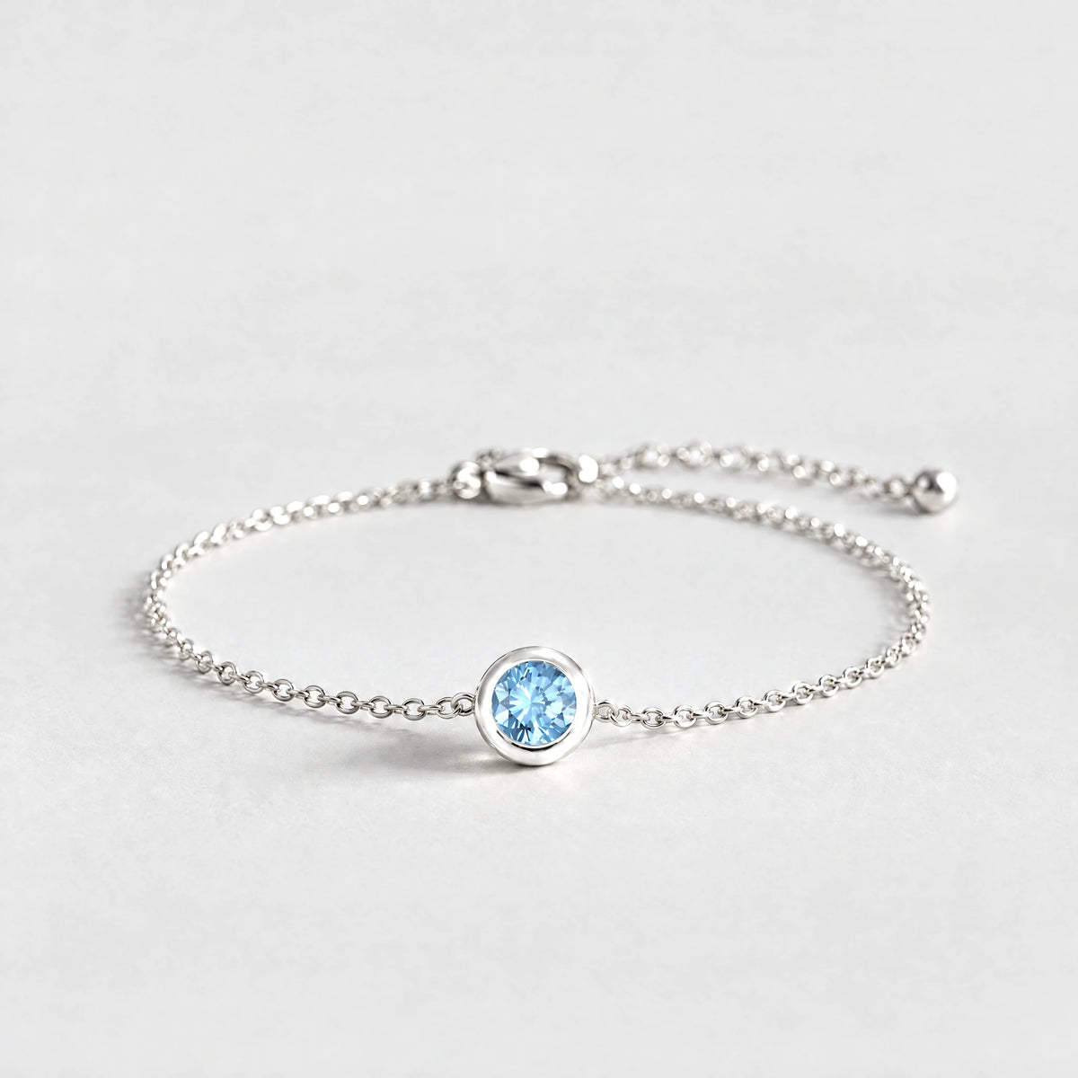 Silver Zara Birthstone Charm Bracelet with aquamarine blue March birthstone-color crystal on a light grey background