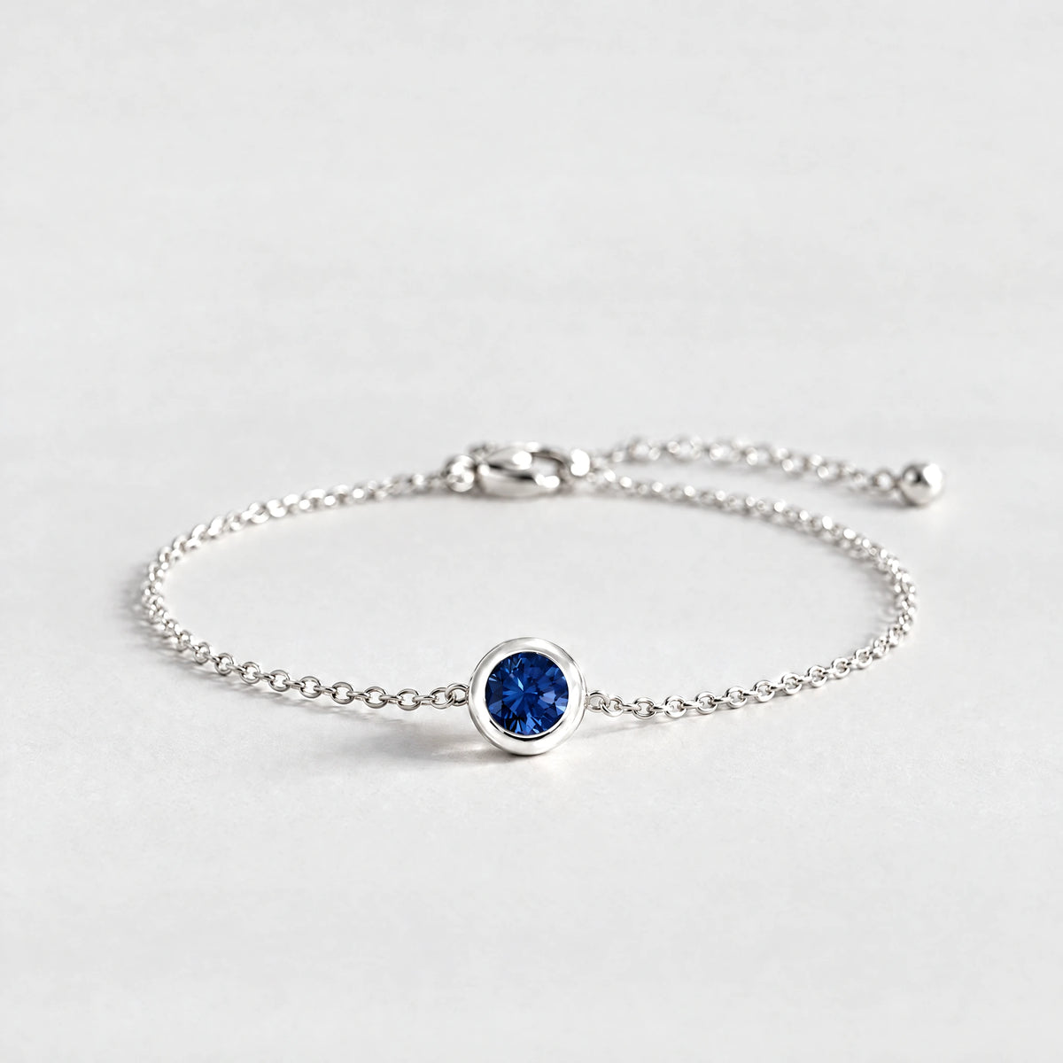 Silver Zara Birthstone Charm Bracelet with sapphire blue September birthstone-color crystal on a light grey background